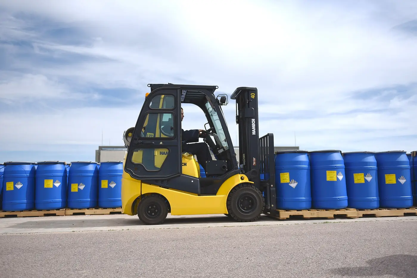 Forklift carrying blue steel drums across a yard